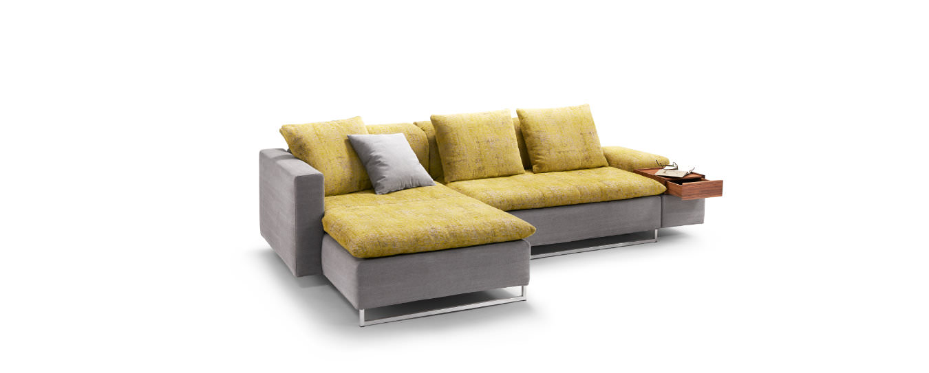 Isla Ecksofa von Signet – Modern in Grau und Gelb. Isla Ecksofa von Signet in grauem Korpus mit gelben Kissen und eleganten Edelstahlfüßen.